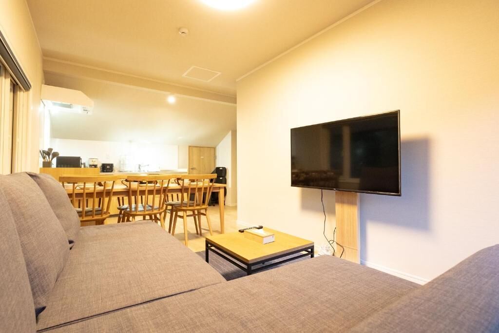 A living room with a sofa, a coffee table, and a TV mounted on the wall.