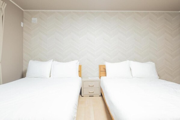 A hotel room with two single beds, a small bedside table with drawers, and a herringbone-patterned wall. - VILLA LOUISA (Furano)