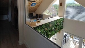 A modern loft bedroom with a sloped ceiling, a built-in kitchen, and a view of the outdoors. - Le Dreispitz : Gîte d'Exception in Alsace (Gresswiller)