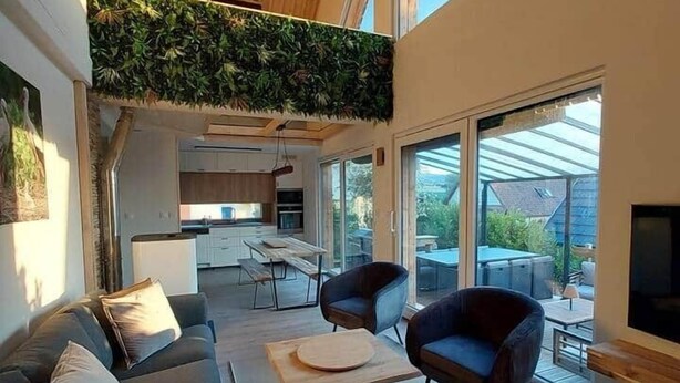 A modern living room with a high ceiling, a built-in green wall, and large windows offering a view of the outdoors. - Le Dreispitz : Gîte d'Exception in Alsace (Gresswiller)