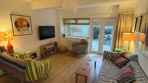 A living room with a sofa, a chair, a television, a fireplace, and a view to the outside.