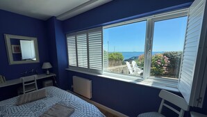 A bedroom with a large window, a bed, a chair, a desk, and a radiator.