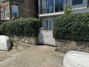A residential building with a white picket fence, a stone wall, and a concrete pathway leading to a door. - Quay Rocks, wonderful three bedroom ground floor holiday home with sea views (Seaview)