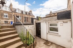 A narrow alleyway with a white building on the right, a black gate, and a metal staircase leading up. - Melbourne Place (No 23) (St Andrews)