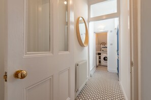 Ein Flur mit einem gemusterten Boden, einem Heizkörper, einem spiegelnden Holzrahmen und Blick in einen Hauswirtschaftsraum mit Waschmaschine und Trockner.