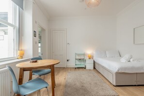 A bedroom with a bed, bedside table, lamp, and a window. - Melbourne Place (No 23) (St Andrews)
