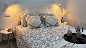 Camera da letto con copriletto decorato, opere d'arte a parete, lampade sui comodini, un piccolo tavolo con vassoio e una pianta da comodino.