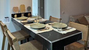 Zona pranzo con un lungo tavolo apparecchiato per sei persone, circondato da sedie in vimini, illuminato da tre lampade a sospensione in vimini.