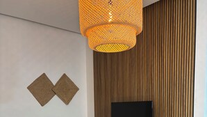 Un soggiorno moderno con un divano, due tavolini, una televisione montata su una parete in legno e una lampada a sospensione.