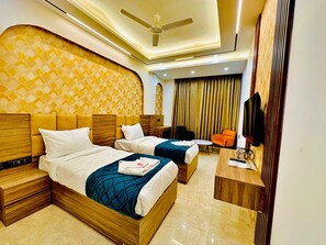 A hotel room with two beds, a desk, a chair, a TV, and a ceiling fan. - Hotel Armani-Free Airport Pickup Aur Drop (New Delhi)