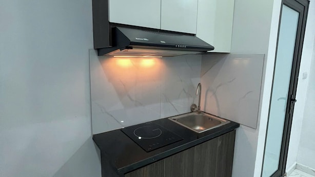 A compact kitchen with a built-in stove, a sink, and a black range hood. - HB Apartment Kim Ma (Hanoi)