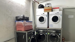 A laundry area with stacked washing machines and a cart with a suitcase. - HB Apartment Kim Ma (Hanoi)