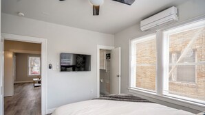 A bedroom with a bed, a TV mounted on the wall, and a window with blinds. - Furnished 1BR Near Downtown & UH – Monthly OK (Houston)