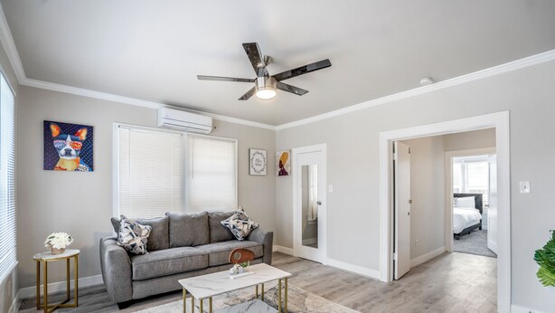 A modern living room with a grey sofa, a white coffee table, and a ceiling fan. - Furnished 1BR Near Downtown & UH – Monthly OK (Houston)