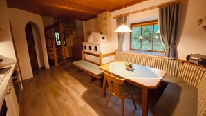 A cozy room with a wooden table, bench seating, a stone fireplace, and a window with curtains. - Vacation home with garden Carinthia (Kötschach - Mauthen)