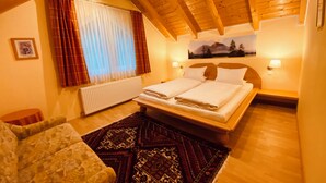 A cozy bedroom with a wooden ceiling, a bed with white linens, a patterned rug, and a window with curtains. - Vacation home with garden Carinthia (Kötschach - Mauthen)