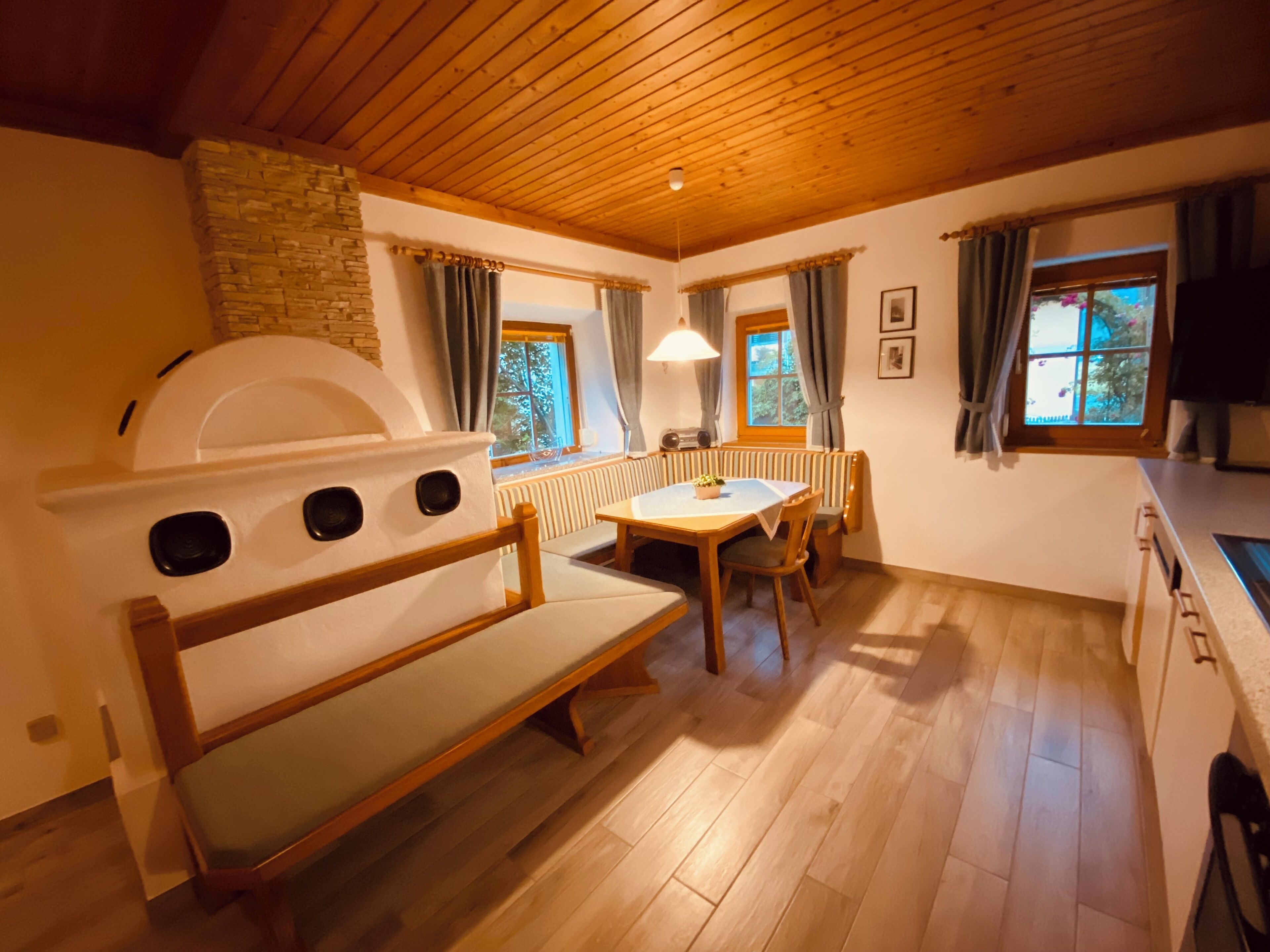 Ein gemütliches Zimmer mit einer Holzbank, einem Tisch mit Stühlen, einem Heizkörper und einem Fenster mit Vorhängen.