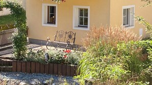A yellow building with a balcony, a hanging flower basket, and a garden with a wooden fence. - Vacation home with garden Carinthia (Kötschach - Mauthen)