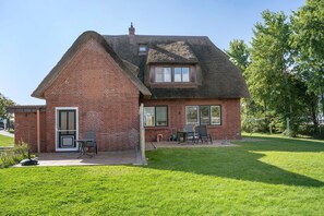 Una casa con fachada de ladrillo, tejado de paja y un pequeño patio con muebles de exterior.