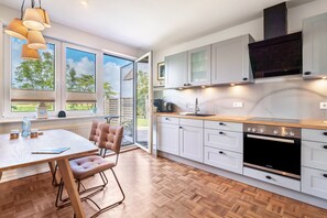 Une cuisine moderne avec des meubles blancs, un plan de travail en bois et une grande fenêtre donnant sur un jardin.