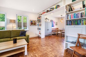 Una sala de estar moderna con un sofá verde, piso de madera, una mesa de centro y una estantería llena de libros.