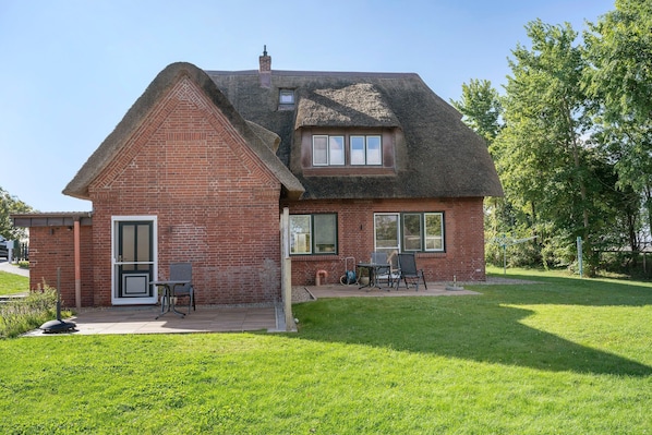 A house with a brick exterior, a thatched roof, and a small patio area with outdoor furniture.