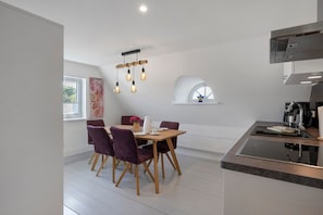 Una cocina moderna con estufa integrada, un comedor con mesa y sillas, y una lámpara colgante.