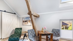 A room with a wooden ceiling beam, a sliding barn door, a dining table with chairs, and a view through a window.