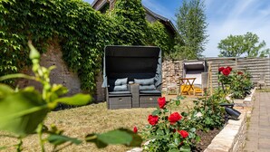 A garden with a wicker sofa, a stone wall, and a brick pathway.