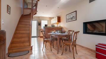Un escalier menant à un espace repas avec des chaises et une table en bois, une cuisine en arrière-plan et une boîte de rangement rouge.