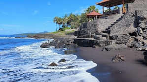 Une plage avec un escalier en pierre menant à une structure traditionnelle en bois, surmontée d’un toit rouge.