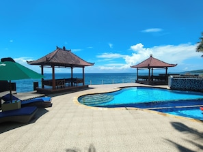 A pool area with two gazebos, lounge chairs, and a view of the ocean. - Kebun Impian Guesthouse (Karangasem)