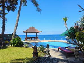 A pool area with a gazebo, lounge chairs, and a statue. - Kebun Impian Guesthouse (Karangasem)