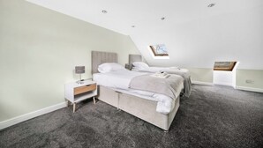 Une chambre avec un plafond en pente, deux lits, une table de chevet, un bureau et une lucarne.