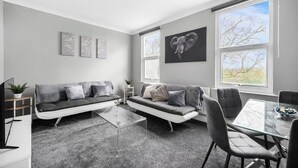 Un salon moderne avec un canapé gris, une table basse en verre et un coin repas comprenant une table et des chaises en verre.