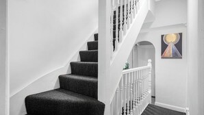 Un escalier avec des marches recouvertes d’une moquette sombre et des balustrades blanches.