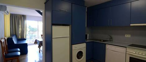 Una cocina compacta con armarios azules, lavadora, lavavajillas y estufa.