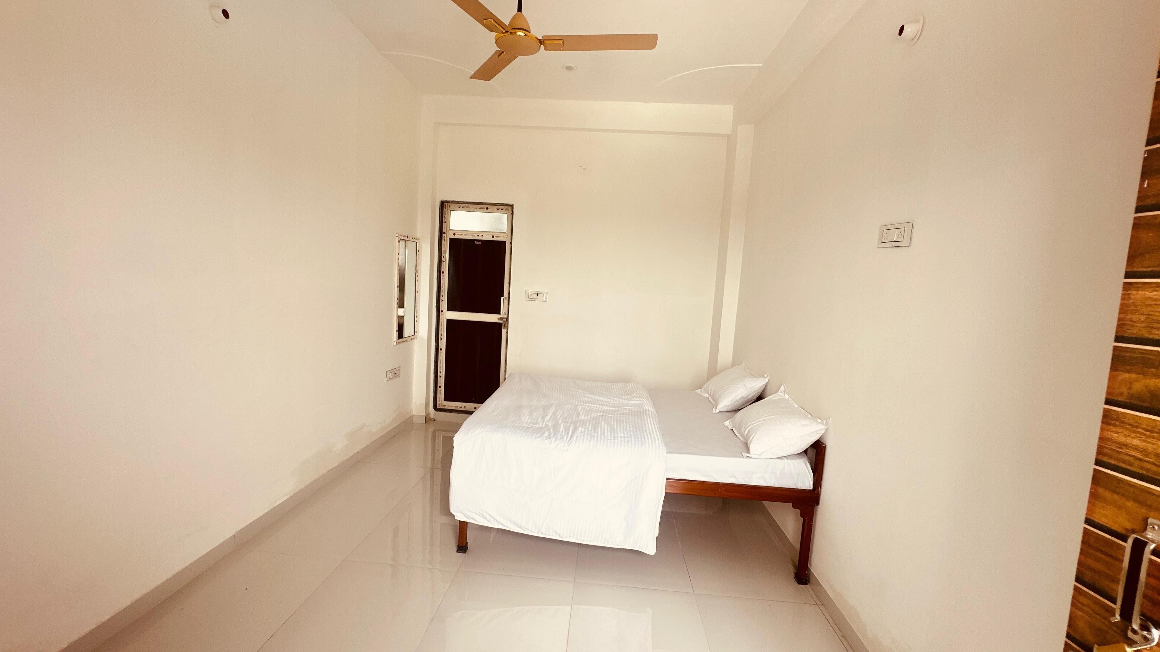 A narrow hallway leading to a bedroom with a bed, a ceiling fan, and a door.