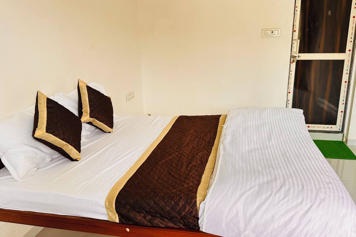 Una cama con ropa de cama blanca y marrón, estructura de madera y un felpudo verde al pie.