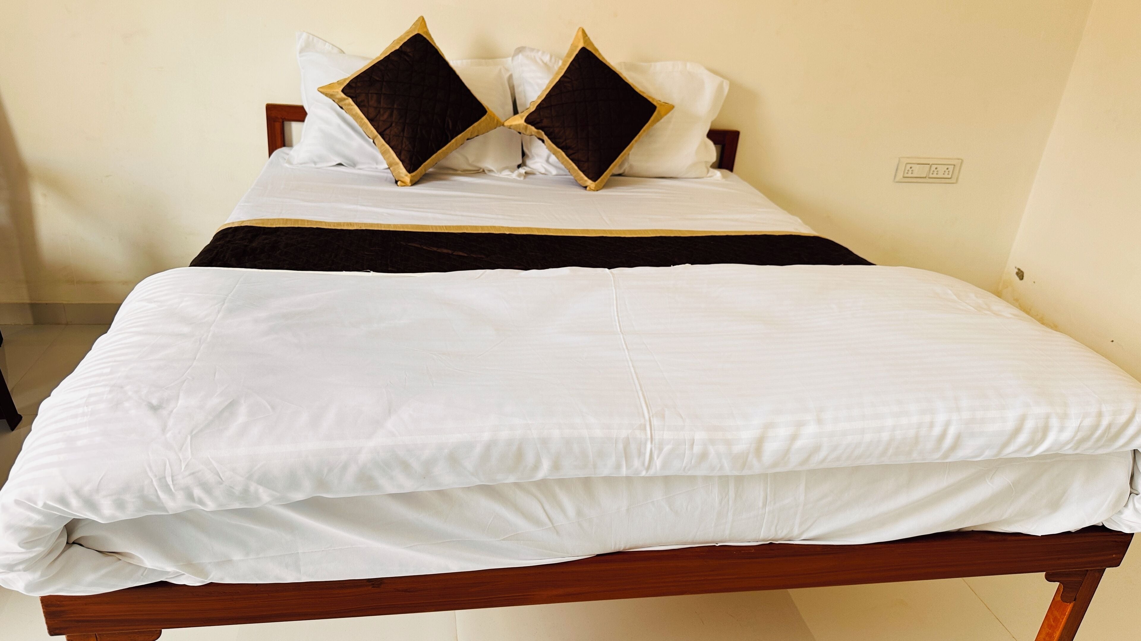 A neatly made bed with white bedding and two decorative pillows with a black and gold design.