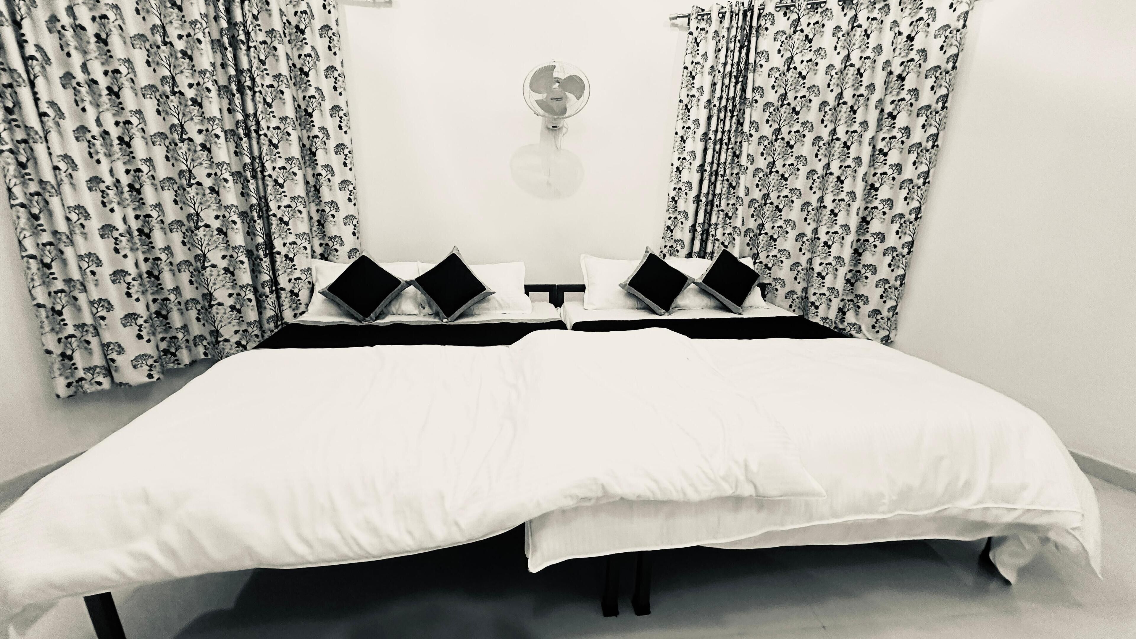 Una cama doble con un edredón blanco, dos almohadas negras y una mesita de noche con una lámpara.