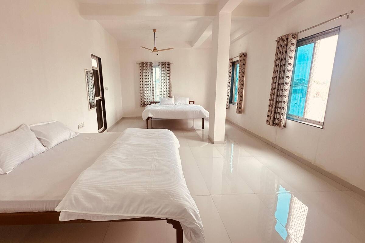 Habitación de hotel con una cama grande, una cama más pequeña, un ventilador de techo y una ventana con cortinas estampadas.