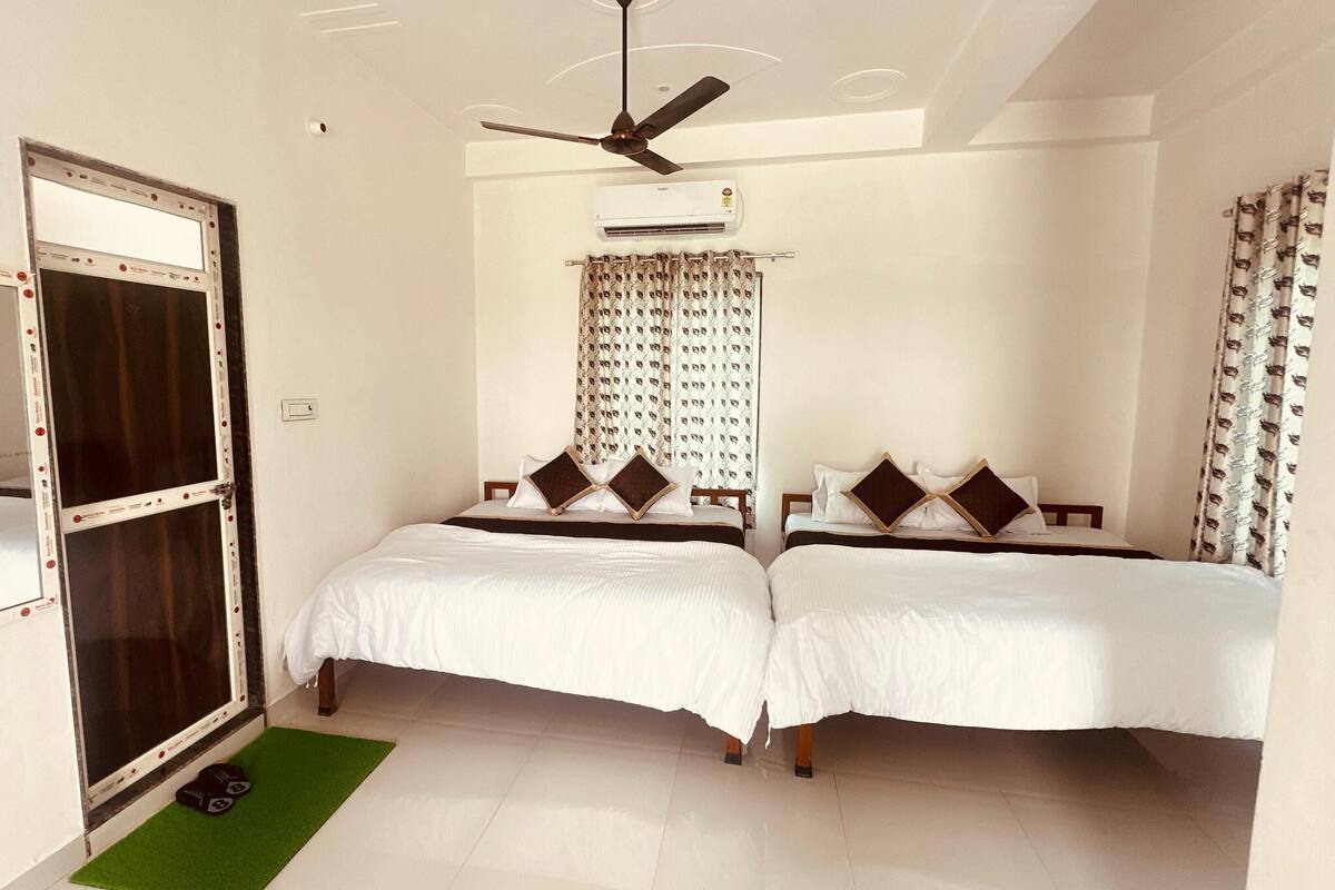 Habitación de hotel con dos camas, ventilador de techo, aire acondicionado y un felpudo verde en la entrada.