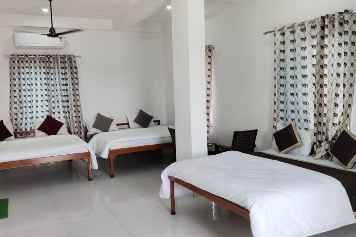 Habitación de hotel con dos camas individuales, un escritorio y una silla. Incluye ventilador de techo, unidad de aire acondicionado y cortinas estampadas.