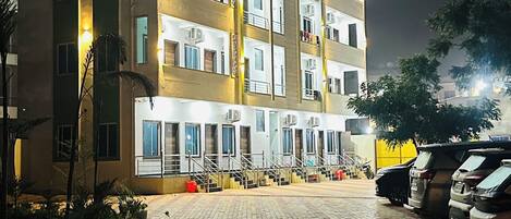 Un hotel a più piani con un ingresso lastricato e un'area di parcheggio.