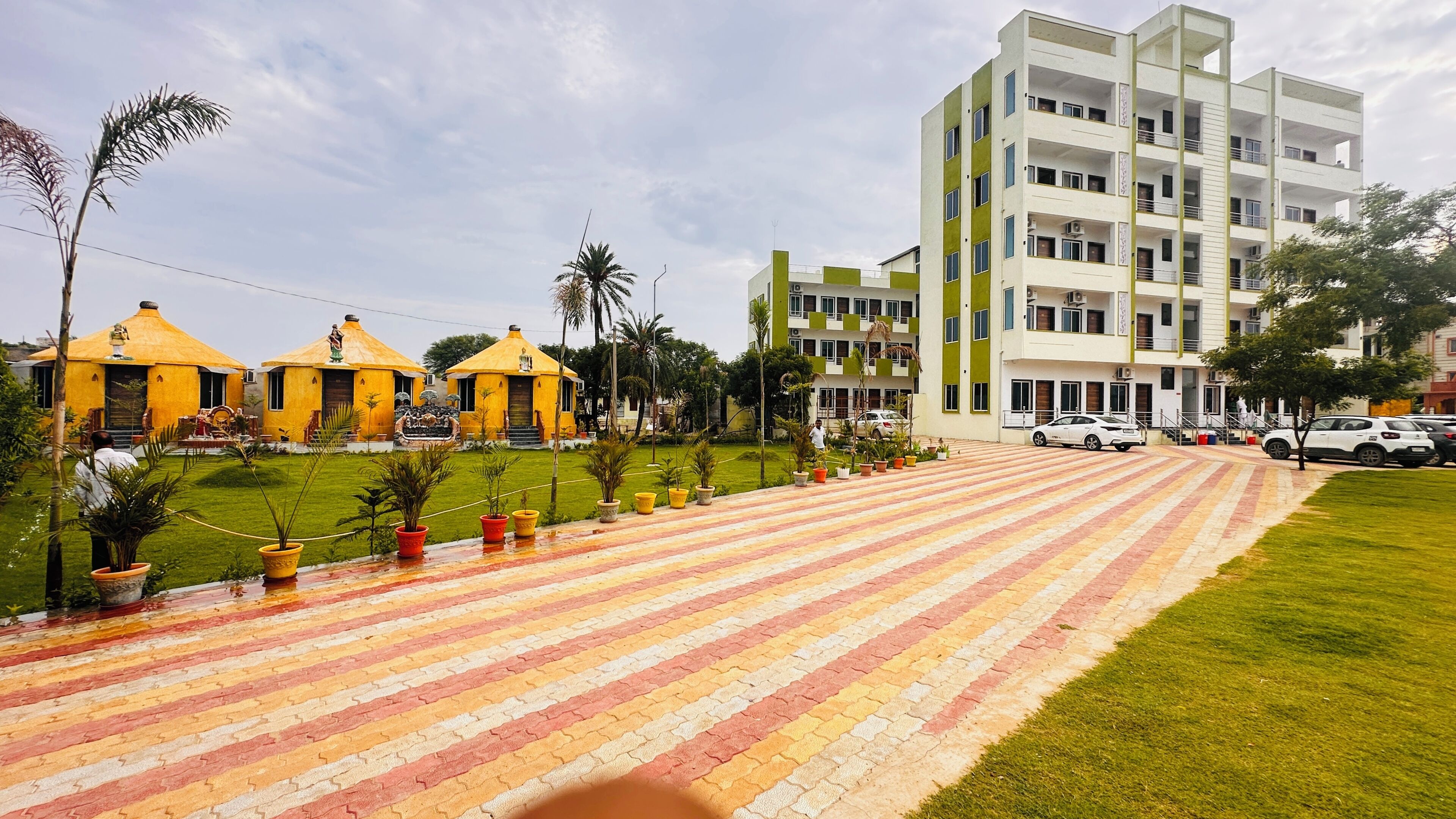 A building with multiple floors, a paved area with potted plants, and a grassy lawn.