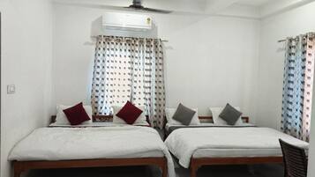 A room with two single beds, a ceiling fan, an air conditioning unit, and patterned curtains.
