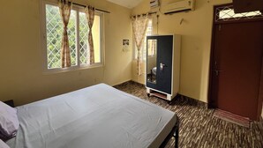 Una habitación con cama, armario, ventilador de techo, aire acondicionado y ventana con cortinas.