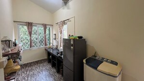 A compact kitchen with a refrigerator, a washing machine, a window with curtains, and a ceiling fan.