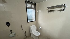 A bathroom with a toilet, a window, a towel rack, and a shower.